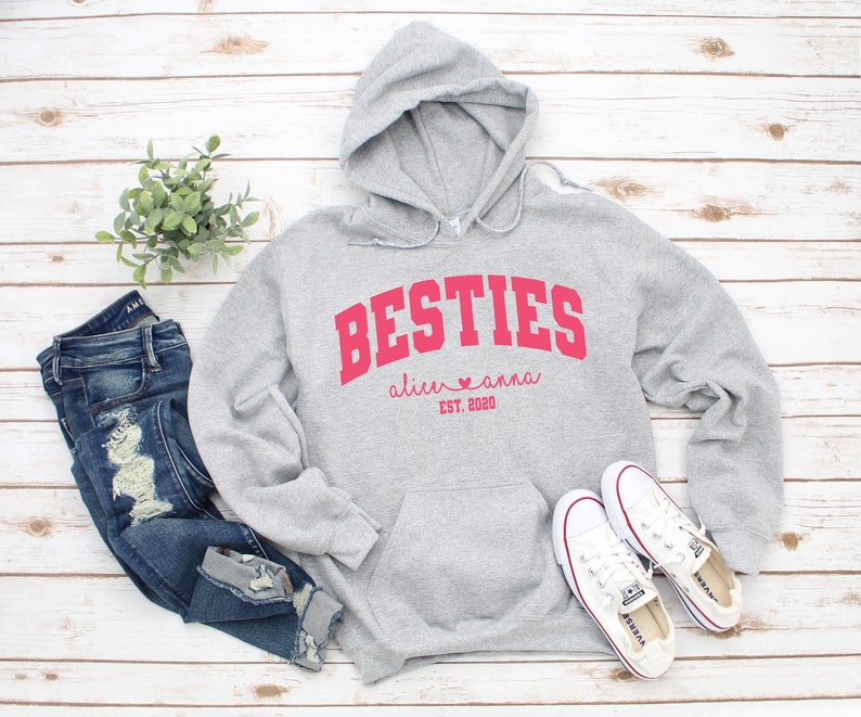 May include: Gray hooded sweatshirt with the text "BESTIES" in red, with the names "alice" and "anna" and the date "EST. 2020" underneath.