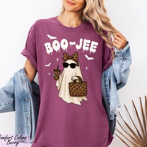 A woman wearing a purple t-shirt with a graphic of a ghost holding a drink and sunglasses, along with the text "BOO JEE" and leopard print accessories.