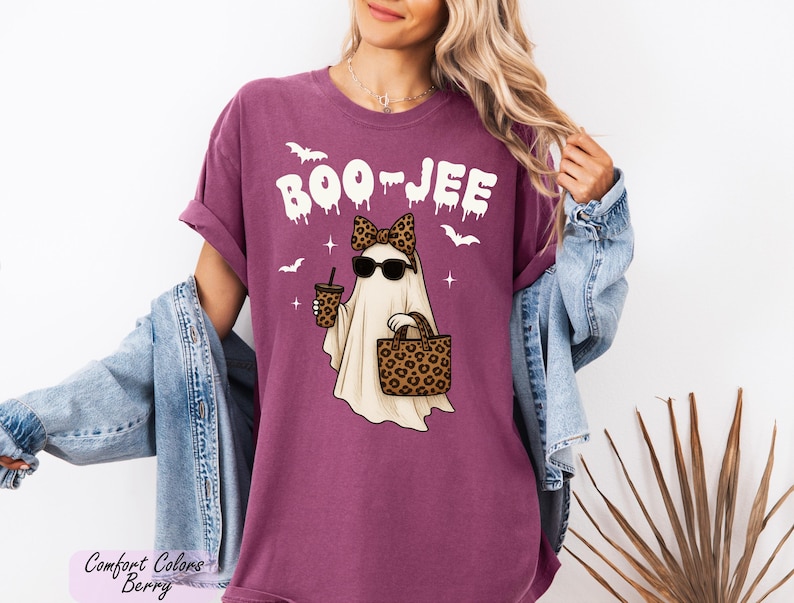 A woman wearing a purple t-shirt with a graphic of a ghost holding a drink and sunglasses, along with the text "BOO JEE" and leopard print accessories.