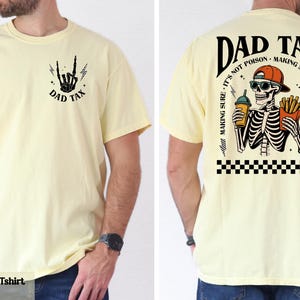 A yellow t-shirt with a graphic design on the back, depicting a skeleton wearing a baseball cap and holding a beer.