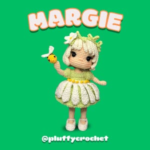 Puede incluir: Una muñeca de crochet llamada Margie, vestida con un vestido de margarita blanco y verde, sosteniendo una abeja amarilla y negra. La muñeca tiene el pelo rubio y los ojos marrones. El fondo es verde.