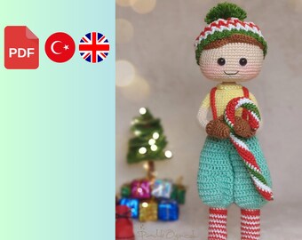 Puede incluir: Patrón de muñeca amigurumi de elfo de crochet en formato PDF. El elfo lleva un gorro a rayas verde y blanco, una camisa a rayas verde y blanco, pantalones verdes y calcetines a rayas rojo y blanco. El elfo sostiene un bastón de caramelo.