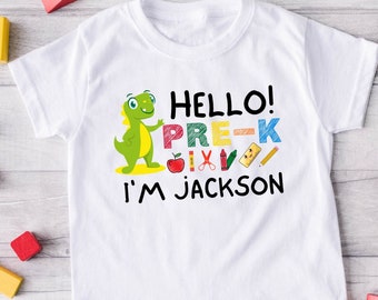 Op de afbeelding: Wit T-shirt met een groene dinosaurus afbeelding en de tekst "Hello! Pre-K I'm Jackson".