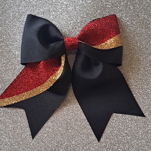 May include: A black and red cheer bow with gold glitter trim. The bow is made of grosgrain ribbon and has a large, full shape.