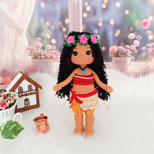 May include: Crocheted doll with brown hair, wearing a flower crown, a red and white top, and a yellow skirt with a brown sash. The doll is standing on a white surface.