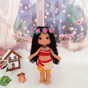 May include: A crocheted doll with brown skin, black curly hair, and a flower crown. The doll is wearing a red and orange top and a yellow and white skirt.