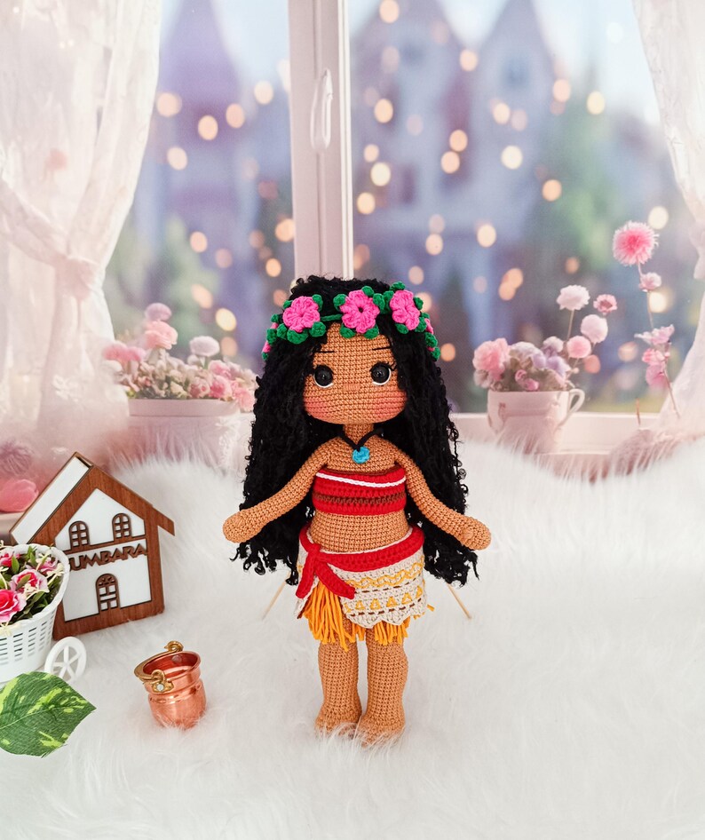May include: A crocheted doll with brown skin, black curly hair, and a flower crown. The doll is wearing a red and orange top and a yellow and white skirt.
