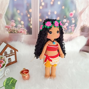 May include: A crocheted doll with brown skin, black hair, and a flower crown. She is wearing a red and white top, a yellow skirt, and a blue necklace.