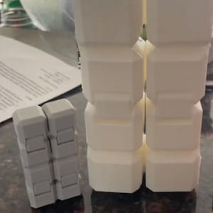 May include: Two white, 3D printed, cube-shaped fidget toys. The larger toy is stacked in a tower of four cubes. The smaller toy is made of two cubes.
