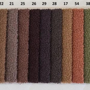 May include: A color swatch card featuring a variety of fabric samples in a range of colors. The samples are arranged vertically and include shades of white, beige, brown, green, and gray. The word "QUELLE" is printed vertically on the left side.