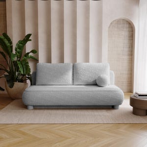 Könnte beinhalten: Ein hellgraues Zweisitzer-Sofa mit abgerundetem Design und einem strukturierten, plüschigen Stoff. Das Sofa hat zwei Rückenkissen und ein rundes Zierkissen. Der Raum verfügt über eine neutrale Farbpalette mit einer großen Topfpflanze und einem kleinen Beistelltisch.