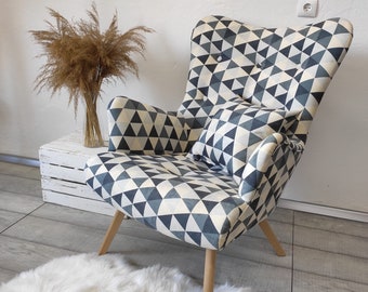 May include: A gray and white geometric patterned armchair with wooden legs. The chair has a matching pillow and is sitting on a white fluffy rug.