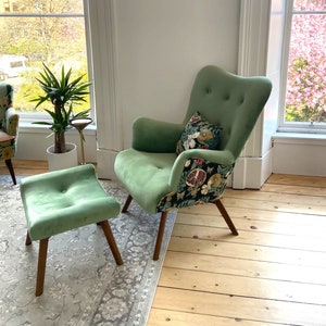 Può includere: Una poltrona in velluto verde con un cuscino a motivi floreali e un poggiapiedi in velluto verde abbinato. La poltrona e il poggiapiedi hanno gambe in legno e sono su un tappeto a motivi.