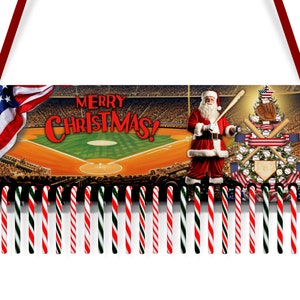 Peut inclure: Une décoration de Noël représentant un terrain de baseball avec un Père Noël tenant une batte de baseball et un sapin de Noël décoré de balles de baseball et de drapeaux américains. La décoration est ornée d'une frange de cannes en sucre rouge, blanche et verte. Le texte "Merry Christmas!" est affiché sur la décoration.