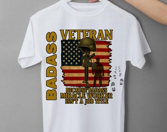 May include: White t-shirt with a graphic design featuring the word "BADASS" vertically, and "VETERAN" above an American flag design. The text "BECAUSE BADASS MIRACLE WORKER ISN'T A JOB TITLE" is also included.