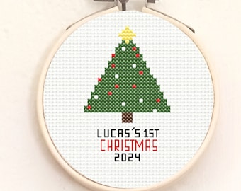 May include: A green and white cross-stitch design of a Christmas tree with red ornaments and a yellow star on top. The text "Lucas's 1st Christmas 2024" is below the tree.