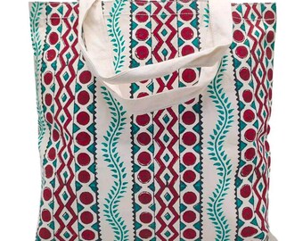 May include: A white canvas tote bag with a colorful geometric pattern. The pattern features red, teal, and black geometric shapes and lines. The bag has two white canvas straps.