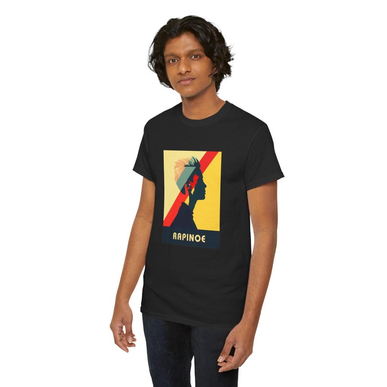 May include: A black t-shirt with a graphic of a person's silhouette with a yellow, red, and blue design. The text "RAPINOE" is printed below the graphic.
