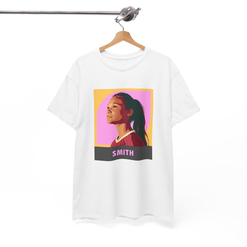 May include: White t-shirt with a graphic of a woman with brown hair and a pink and yellow background. The text "SMITH" is printed in black below the graphic.