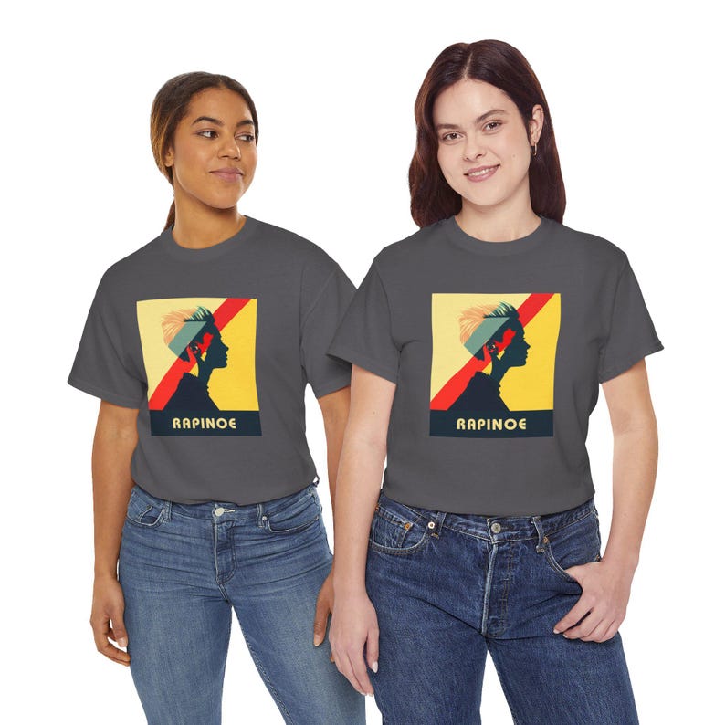 May include: Two people wearing charcoal gray t-shirts with a graphic of a woman's silhouette with the text "RAPINOE" printed below. The graphic is in a retro style with red, yellow, and blue colors.