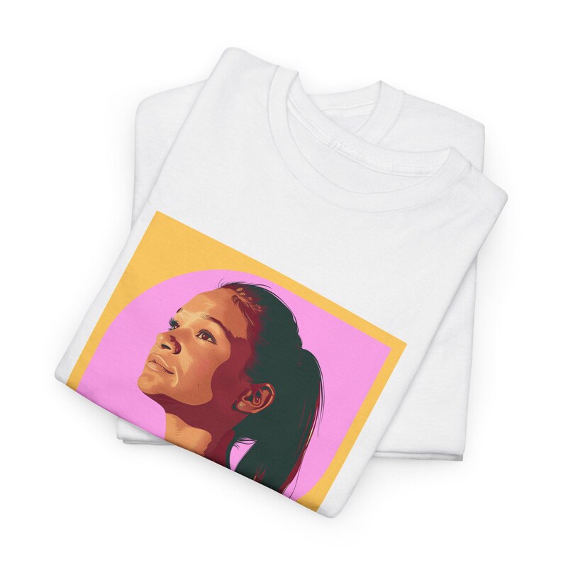May include: White t-shirt with a graphic of a woman's face with a pink and yellow background.