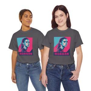 May include: Two people wearing charcoal gray t-shirts with a pink and blue graphic of a woman's face and the text "The Morgan" printed on the front.