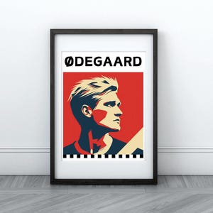 May include: A framed poster with a red, white, and blue color scheme. The poster features a stylized illustration of a man with blond hair and a black and white striped shirt. The text "ODEGAARD" is printed in black at the top of the poster.
