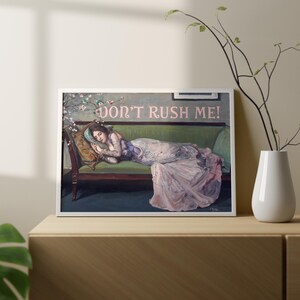 May include: A painting of a woman lying on a green velvet couch with a floral pattern on the wall behind her. The woman is wearing a long, flowing pink dress and has her eyes closed. The text "DON'T RUSH ME!" is written in pink letters above her head.
