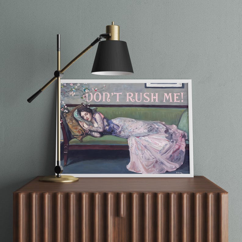 May include: A framed print of a painting depicting a woman in a pink dress lying on a green couch. The woman is asleep and has her head resting on a pillow. The text "DON'T RUSH ME!" is written in pink letters above the couch.