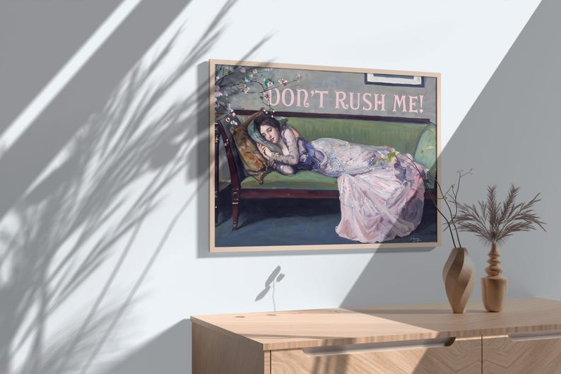 May include: A framed painting of a woman lying on a green couch with the text "Don't Rush Me!" in pink letters. The woman is wearing a pink dress and has her head resting on a pillow. The painting is set against a white wall with a shadow of a plant.