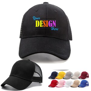 Op de afbeelding: Een zwarte mesh truckercap met een zwarte klep en een witte mesh achterkant. De pet heeft de tekst "Your DESIGN Here" in kleurrijke letters op de voorkant.