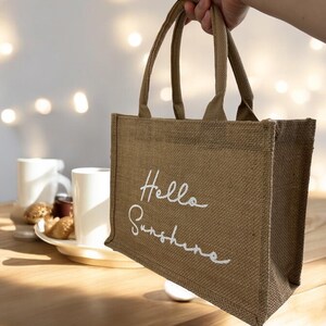 May include: A brown burlap tote bag with white lettering that says "Hello Sunshine".