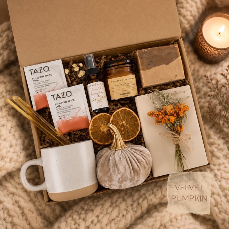 May include: A gift box containing two Tazo Pumpkin Spice Chai tea bags, a small spray bottle, a jar candle labeled Pumpkin Ginger, a rectangular soap bar, a white ceramic mug, two dried orange slices, a velvet pumpkin, and a small dried flower bouquet.