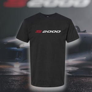Op de afbeelding: Zwart T-shirt met een witte "S2000" grafische afbeelding in rode letters. Het shirt heeft een klassieke ronde hals.
