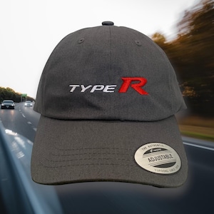 May include: A charcoal gray baseball cap with the text "TYPE R" embroidered in white and red. The cap has a curved brim and an adjustable strap. A silver tag on the brim reads "ADJUSTABLE".