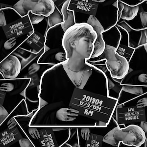 May include: Black and white photo of a person holding a sign that says "201904 12/9/1994 RM". The person is wearing a black shirt and has short, dark hair.