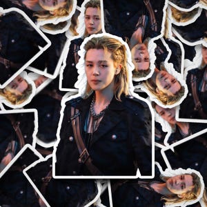 May include: A sticker sheet featuring multiple die-cut images of a person with blonde hair, wearing a black jacket with silver buttons and a layered silver chain necklace. The person has a neutral expression and is shown from the chest up.