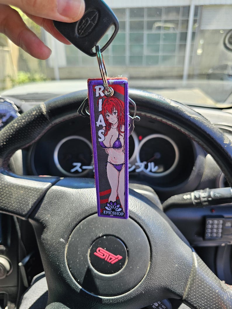May include: A purple keychain with a red and white anime character wearing a bikini. The keychain has the text "RIAS" and "EPICSHOP" on it.