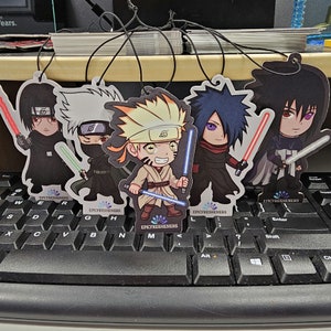 May include: Five colourful car air fresheners featuring anime characters with lightsabers. The characters are Naruto, Sasuke, Kakashi, and two others. The air fresheners are printed with the text "EPICFRESHENERS".