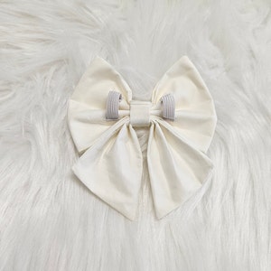 May include: A large, white fabric bow with two elastic bands attached to the back.