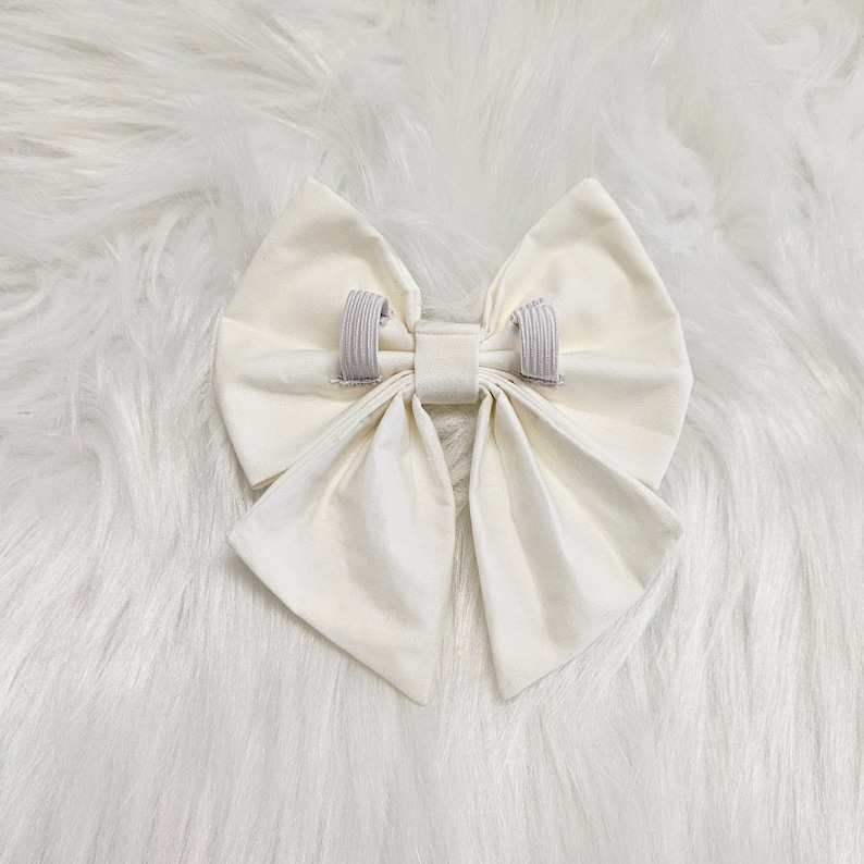 May include: A large, white fabric bow with two elastic bands attached to the back.