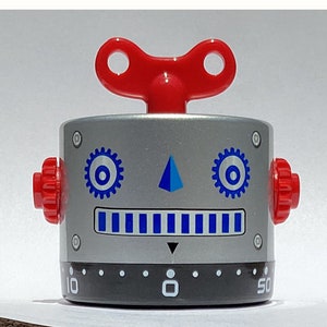 May include: A silver robot-shaped kitchen timer with a red wind-up key on top. The timer has a blue and white face with a blue triangle and two blue gears. The timer has a black dial with numbers from 10 to 50.