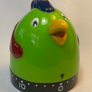 May include: Green plastic kitchen timer shaped like a cartoon chicken with a red wing, blue comb, yellow beak, and black numbers. The timer is set to 10 minutes.