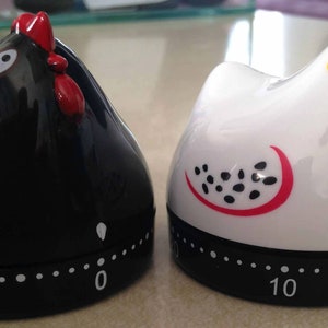 May include: Two ceramic chicken-shaped kitchen timers. One is black with white accents and the other is white with black and red accents. Both timers have a 10-minute countdown.