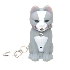May include: A gray and white cat keychain with a light-up feature. The keychain has a silver metal ring.