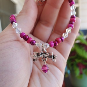 May include: A pink and clear beaded bracelet with a silver bow charm and a pink crystal pendant.