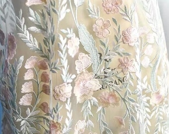 May include: A sheer fabric overlay featuring intricate embroidery of soft pink flowers and sage green foliage. The delicate floral pattern is stitched onto a translucent, lightweight mesh material, creating a layered botanical design.