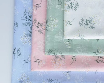 Op de afbeelding: Vier gevouwen stofstalen in lichtblauw, zachtroze, saliegroen en wit. Elk stuk heeft een herhalend botanisch patroon van delicate witte en donkergroene wilde bloemen en dunne verticale strepen die in de textielstructuur zijn geweven.
