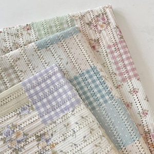 May include: Close-up of four patterned fabric swatches. The fabrics feature floral and gingham patterns in pastel colours, including pink, green, and lavender. The fabrics have a delicate, open weave.