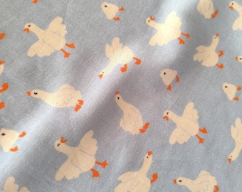 Puede incluir: Tela azul claro con un patrón repetido de gansos blancos con patas y picos naranjas. Los gansos están representados en varias poses, algunos con las alas extendidas, creando un diseño caprichoso. La tela tiene una textura suave y ligeramente arrugada.